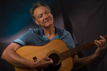 Older Man having fun playing his acoustic guitar against a blue lit backgroundの写真素材