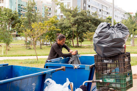 Brasilia, Brazil-March 27, 2020: A Poor Homeless Indigenous Woman Picking through the Trash to find...