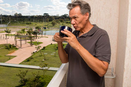 Senior Man Drinking a Cup Coffee Outside on his Balconyの写真素材