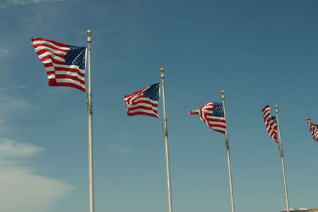 A row of US Flags Flying High on a Pole with a blue sky in the backgroundの写真素材