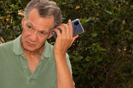 Senior man outside listening to a message on his smartphone