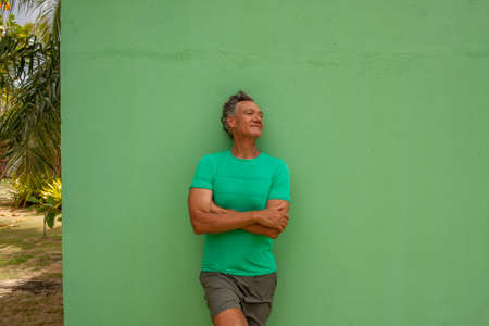 Mature Man relaxing while leaning against a Green Wallの写真素材