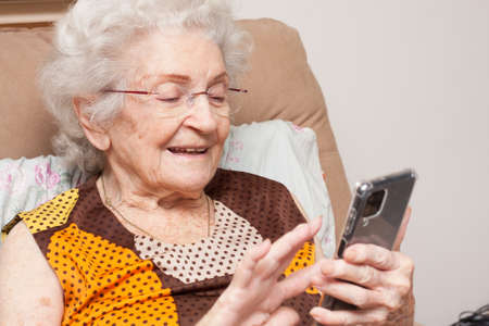Elderly Lady at home sitting in a chair looking at her smartphone