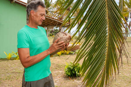 Senior man under a coconut tree holding a coconut that fell from the treeの写真素材