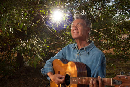 Happy Mature Man singing and playing his acoustic guitar in the park