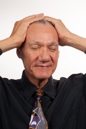 Mature man wearing a black shirt and tie with his hands on his headの写真素材