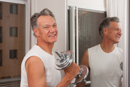 Mature Man 60plus working out with weights at home in front of a mirror doing Bicep Curlsの写真素材