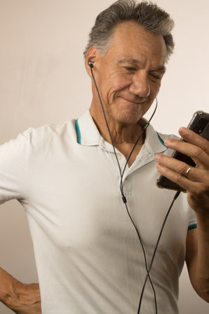 Older man listening to music or a podcast using ear buds on his smart deviceの写真素材