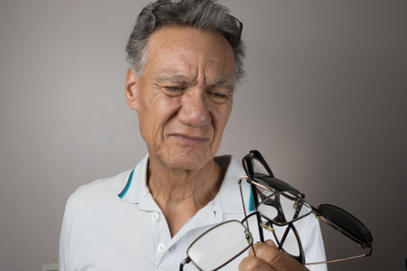 Mature Man checking out and holding up all his old prescription glassesの写真素材