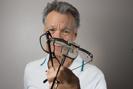 Mature Man checking out and holding up all his old prescription glassesの写真素材