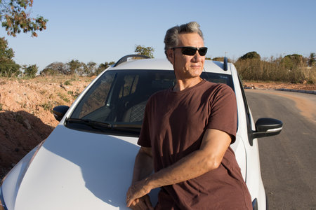 Mature Man taking a break from driving and relaxing and leaning on the hood of his carの写真素材
