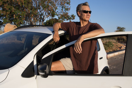 Mature Man taking a break from driving and relaxing and leaning on his car doorの写真素材