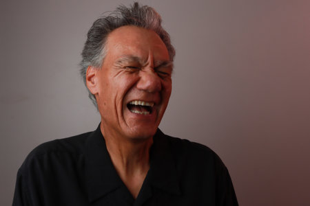 Older Mature Man against a Gray background breaking out in laughterの写真素材
