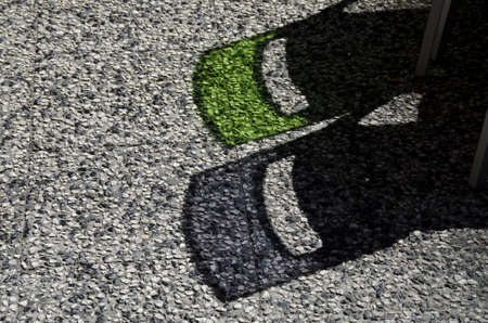 The sun shining down on the shadows of transparent chairs on a stoney pavementの写真素材