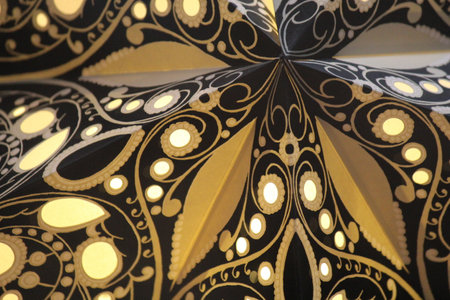 Cut and folded paper with a pattern of gold swirling flowers on dark.