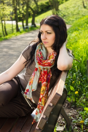 Beautiful young woman sitting on a bench at the park and waiting の写真素材