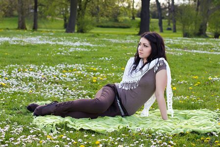 The image of a beautiful girl sitting on the plaid in the parkの写真素材