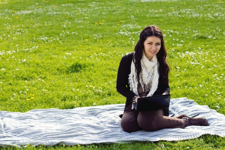 Young woman working with netbook outdoors in park on grassの写真素材