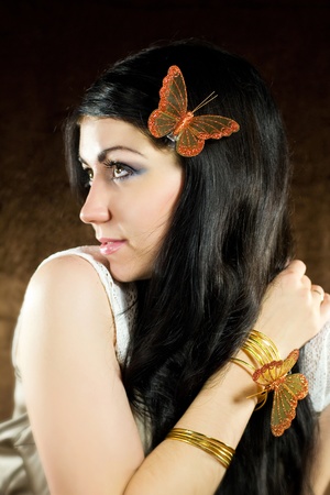 Brunette with brown-gold butterfly against the brown backgroundの写真素材