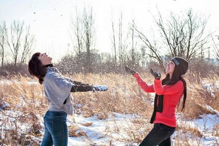 Two female friends walking in park in winter and throwing snowの写真素材