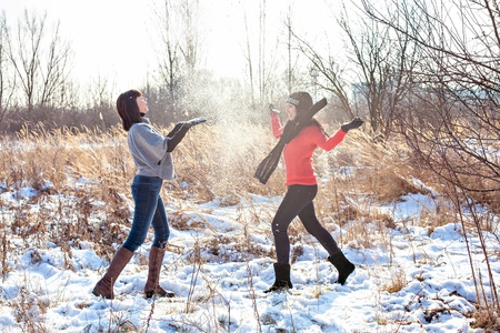 Two female friends walking in park in winter and throwing snowの写真素材
