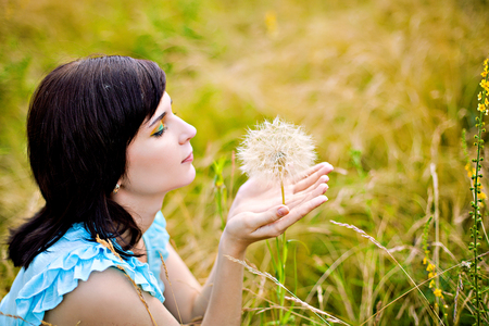 Pretty girl sitting on grass with dandelionの写真素材