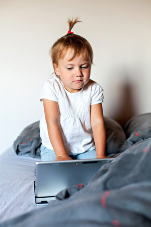 Little girl watching at screen of tablet in the bedの写真素材