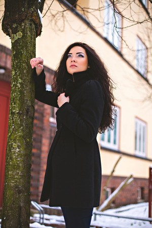 Pretty woman in coat standing near tree on streetの写真素材