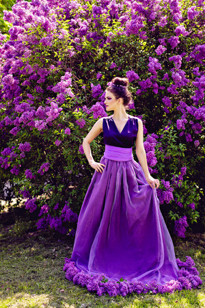 Beautiful girl in lilac ball dress among the flowers in the gardenの写真素材