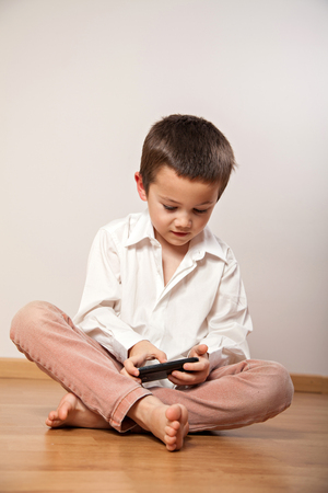 Concentrated little boy playing with mobile phone, smartphoneの写真素材