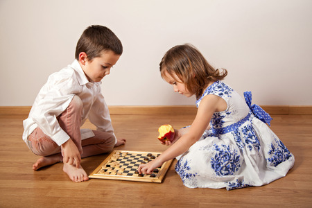 Little birl and boy sitting on the floor and playing chessの写真素材