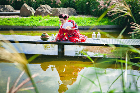 Japanese Geisha woman with fancy makeup in garden with a fanの写真素材