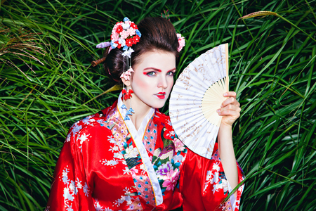 Japanese Geisha woman with fancy makeup in garden with a fanの写真素材