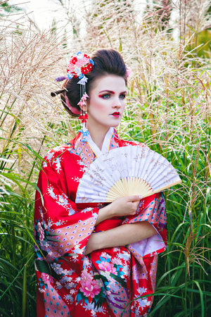 Young woman in geisha costume with fancy makeup in garden with a fanの写真素材