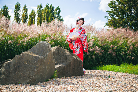 Japanese Geisha woman with fancy makeup in garden with a fanの写真素材