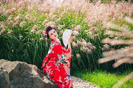 Japanese Geisha woman with fancy makeup in garden with a fanの写真素材