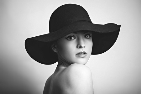 Beautiful young fashionable woman posing in black hat. Vogue style. Black and white photoの写真素材