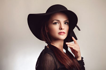 Beautiful young fashionable brunette woman posing in black dress and black hat. Vogue style. Studio photoの写真素材