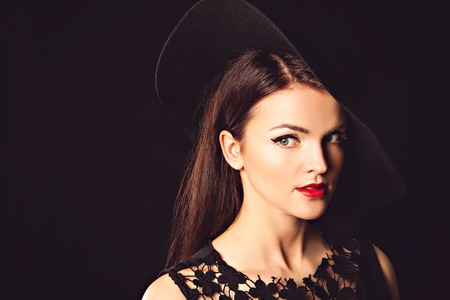 Portrait of a beautiful sexy graceful woman in elegant hat with a wide brim. Red lips. Beauty, fashion concept. Studio photoの写真素材