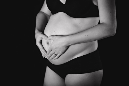 Pregnant woman in black lingerie with heart from hands on her belly