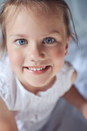 Little cute smiling girl with blue eyes sitting on a bed