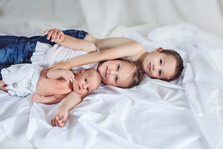 Three cheerful kids at home, newborn baby with brother and sister, happy family, love and friendship...
