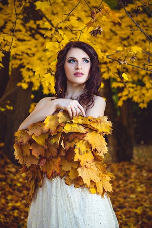Elegant woman wearing a dress, golden leaf shawl looking away on the autumn forest backgroundの写真素材