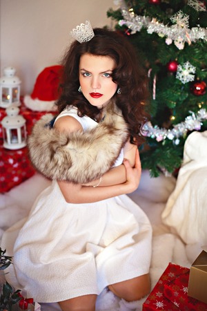 Woman in white festive dress with a crown on head and fur boa on her shoulders on the background of Christmas tree. Studio photoの写真素材
