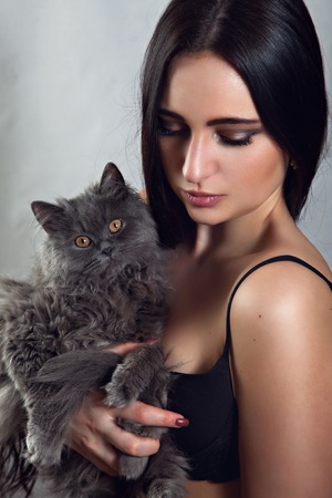 Young woman dressed in black top with persian cat on her armの写真素材