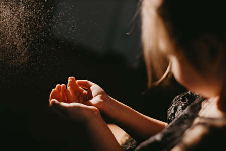 Little girl reaching out for splashing water or spray of perfume in back lightの写真素材