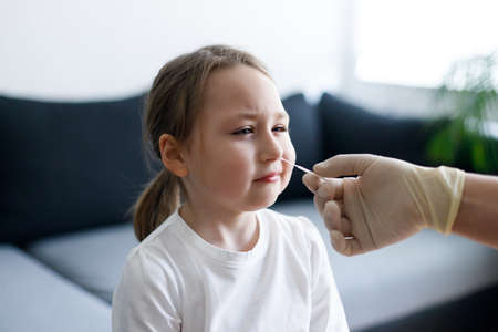 Little girl at home during taking nasal mucus test sample from nose performing respiratory virus testing procedure showing Covid-19の写真素材