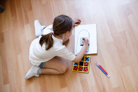 Happy little child is sitting comfortably on the wooden floor, drawing on paper with colored pencils