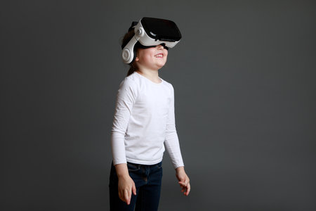Child experiencing virtual reality on gray background. Surprised cute girl looking in VR glasses.の写真素材