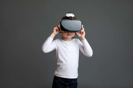 Happy girl wearing virtual reality goggles playing video games looking in VR glasses, child experiencing 3D gadget.の写真素材